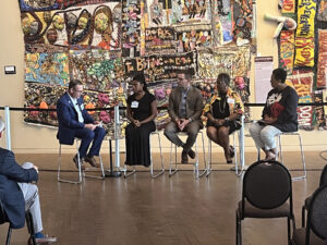 View of four panelists facing a moderator. In the backdrop is a quilt at the Freedom Center Museum.